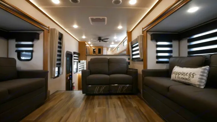 This modern RV rental showcases a spacious living area with two dark gray sofas, wood flooring, and bright lighting.. Forest River Sabre 2021