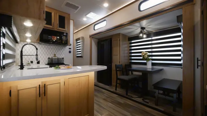 Step inside this RV rental's cozy interior: a modern kitchen with island, microwave, and dining space with table.. Forest River Sabre 2021