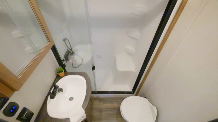 Compact RV rental bathroom features a white sink, clear glass shower, and toilet, designed for space efficiency.. Forest River Sabre 2021