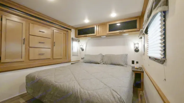 This RV rental bedroom features a comfy bed, built-in storage, wall lights, and blinds, offering a cozy interior.. Forest River Sabre 2021