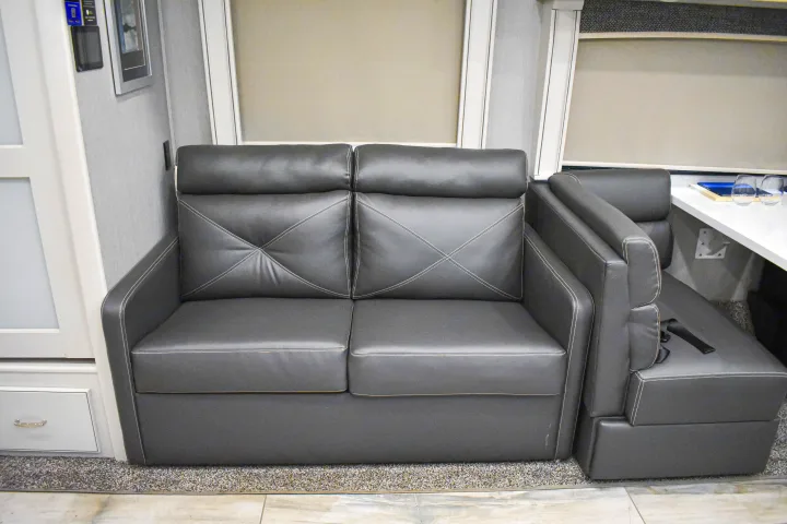 Comfortable gray leatherette sofa in an RV rental, with a dinette section visible, offering cozy seating.. Holiday Rambler Endeavor 2022