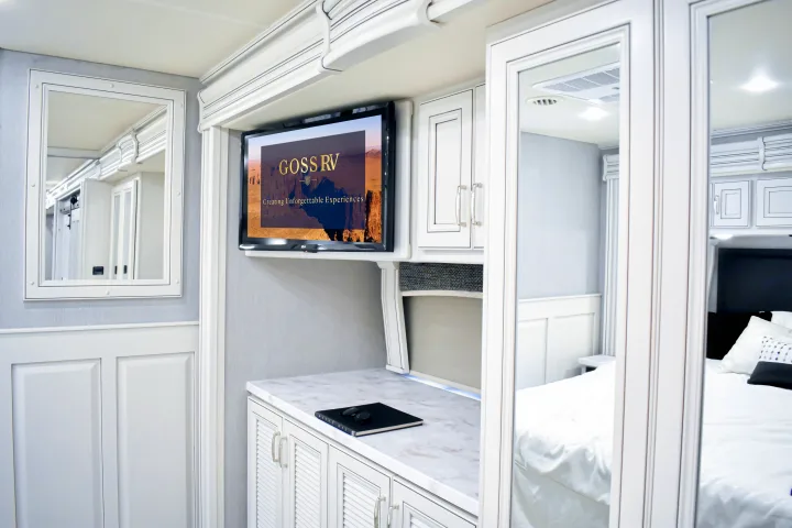 This luxury RV rental features a modern interior with white cabinetry, a TV, and mirrored doors reflecting a comfortable bedroom.. Holiday Rambler Endeavor 2022