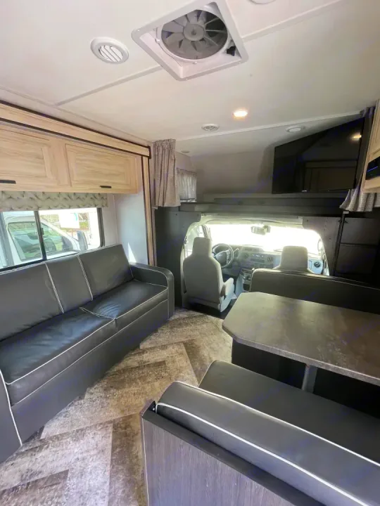Spacious RV rental interior: living area with a sofa, dining booth, overhead bunk, and front cab view.. Forest River Sunseeker 2021