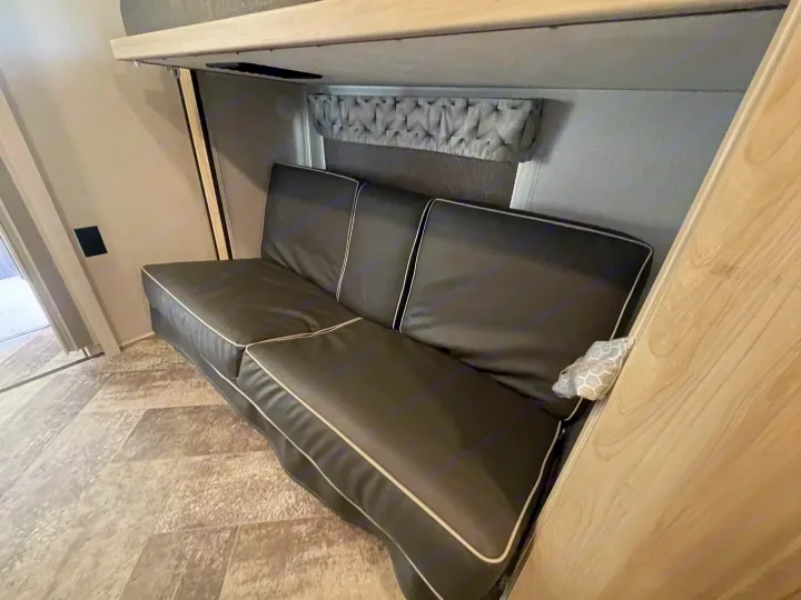 Inside this RV rental, a dark grey sofa with white piping sits beneath an upper bunk bed on patterned flooring.. Forest River Sunseeker 2021