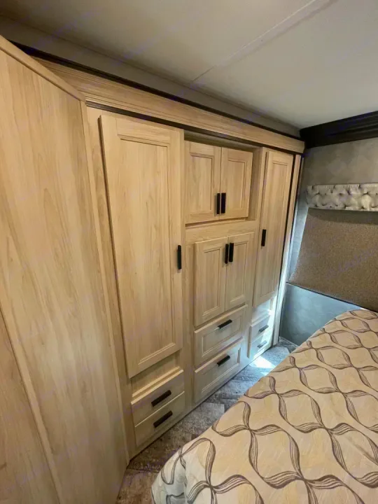 RV rental bedroom interior, showcasing practical light wood wardrobe storage, built-in cabinets, and a cozy patterned bed.. Forest River Sunseeker 2021