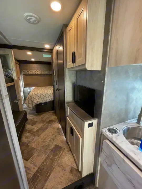 Clean, modern RV rental interior featuring a kitchen sink, mounted TV, and bedroom. Ideal for your next trip.. Forest River Sunseeker 2021