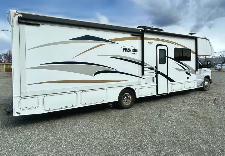 White Phantom by Nexus Class C motorhome with detailed graphics, ready for your next rv rental adventure on a gravel lot.. Nexus Phantom 2018