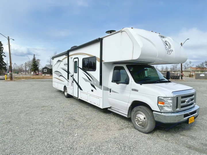 White Nexus Phantom Class C RV rental parked on a gravel lot under a partly cloudy sky, ready for travel.. Nexus Phantom 2018