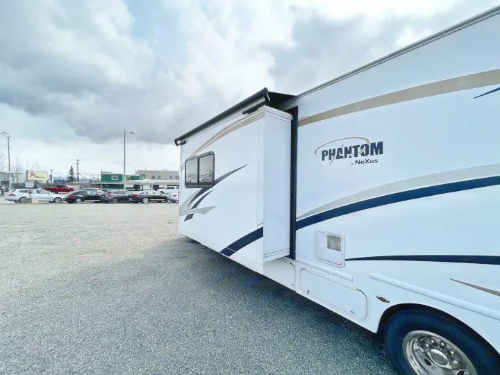 White Phantom by Nexus RV rental with extended slide-out, parked on a gravel lot under cloudy sky.. Nexus Phantom 2018