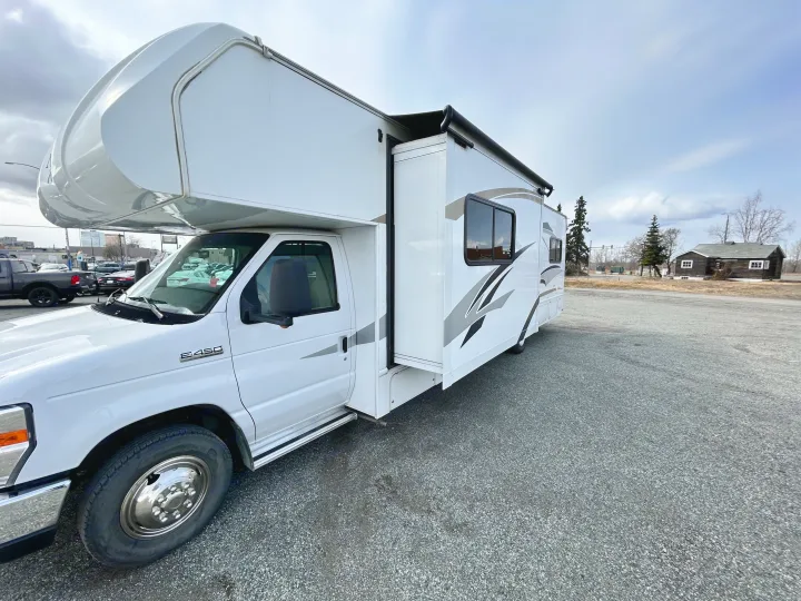 White Class C RV for rv rental, featuring an extended slide-out, parked on a gravel lot under a cloudy sky.. Nexus Phantom 2018