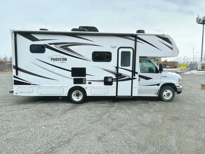 A white Phantom by NeXus Class C motorhome with black & gray graphics, seen parked on a gravel lot. Available for rv rental.. Nexus Phantom 2020