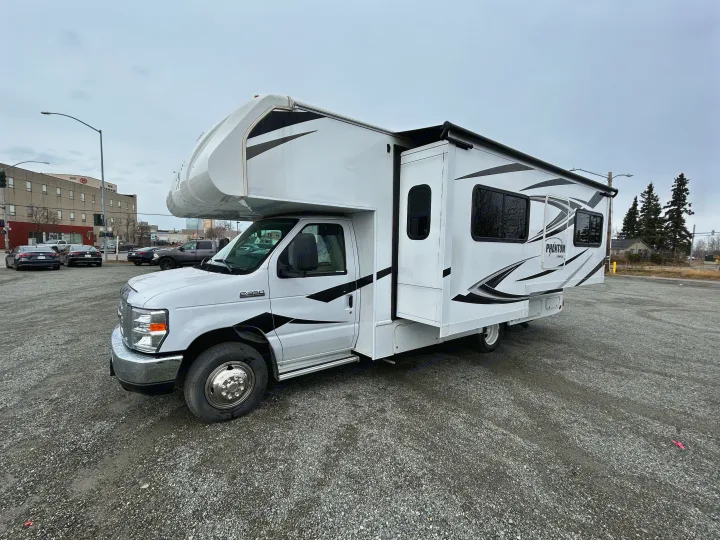 A white Class C RV rental, a Phantom by Nexus, is shown parked on gravel with its slide-out extended.. Nexus Phantom 2020