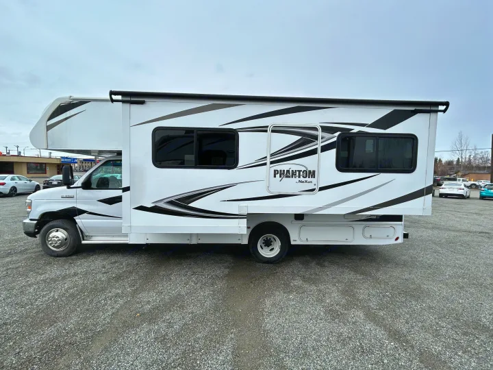 A white Phantom by Nexus Class C RV rental, featuring striking graphics, is parked on a gravel lot, ready for travel.. Nexus Phantom 2020