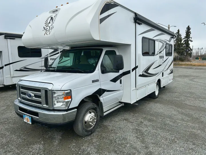 This white Nexus Phantom rv rental, a Ford E-350 Class C, is parked on a wet gravel lot on an overcast day.. Nexus Phantom 2020