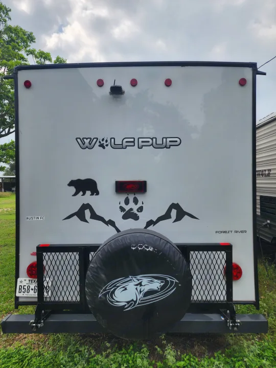 Rear of a white Wolf Pup rv rental by Forest River, showing a spare tire, cargo rack, and Texas license plate.. Forest River Cherokee Wolf Pup Black Label 2022