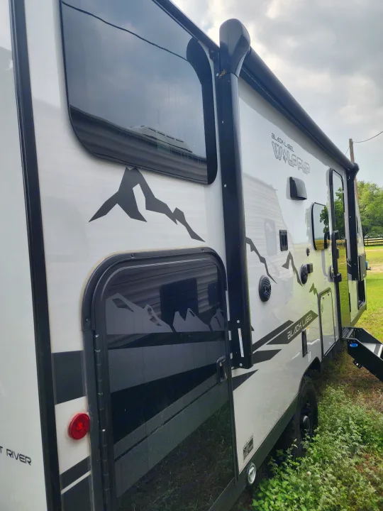 Exterior of a modern white travel trailer with black mountain graphics and an awning. Perfect for your next RV rental.. Forest River Cherokee Wolf Pup Black Label 2022