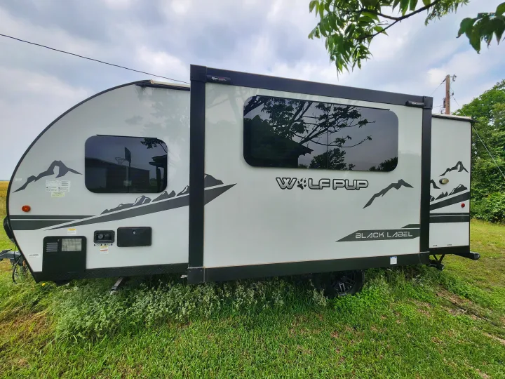 Light grey Wolf Pup Black Label travel trailer RV rental, featuring mountain decals, parked on green grass.. Forest River Cherokee Wolf Pup Black Label 2022