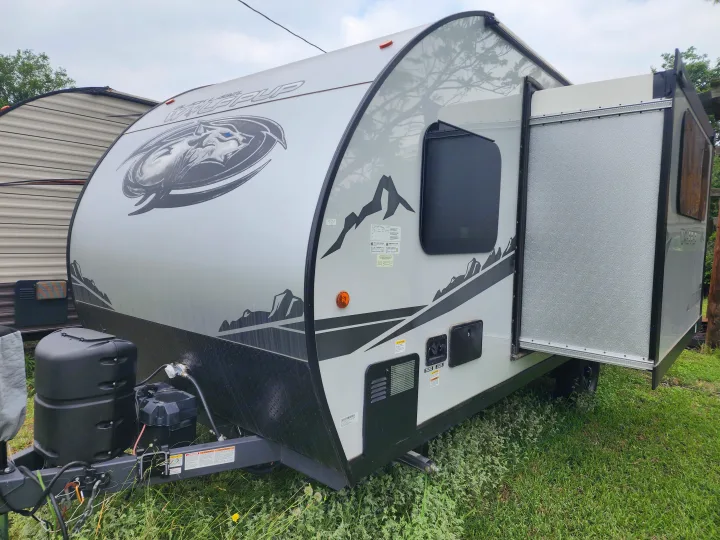 Front view of a light grey Wolf Pup RV rental, with mountain graphics & an open rear bed extension. Ideal for camping.. Forest River Cherokee Wolf Pup Black Label 2022
