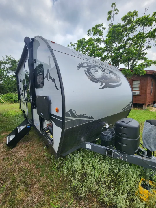 A sleek grey travel trailer, perfect for rv rental, sits on grass. Features propane tanks, steps, and stylish graphics.. Forest River Cherokee Wolf Pup Black Label 2022