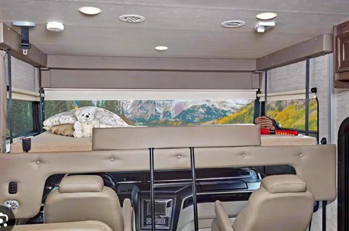 Explore an RV rental's cozy interior, featuring an overhead bunk with a scenic mountain backdrop. Perfect for family adventures.. Entegra Coach Vision 2021