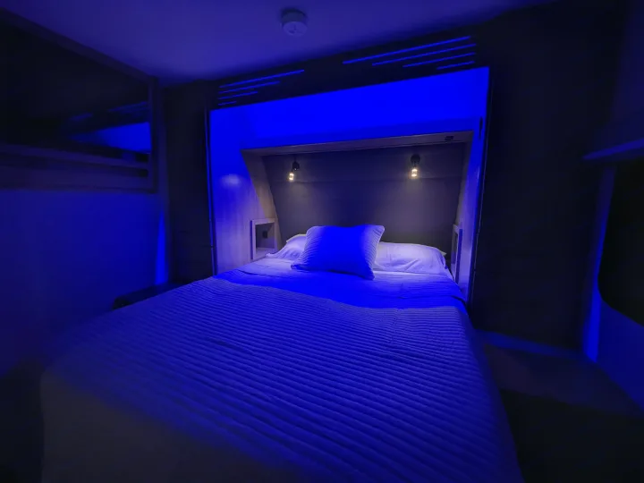 Relax in this RV rental bedroom with vibrant blue LED lighting. Features a comfortable bed, built-in storage, and reading lamps.. Grand Design Imagine XLS 2023