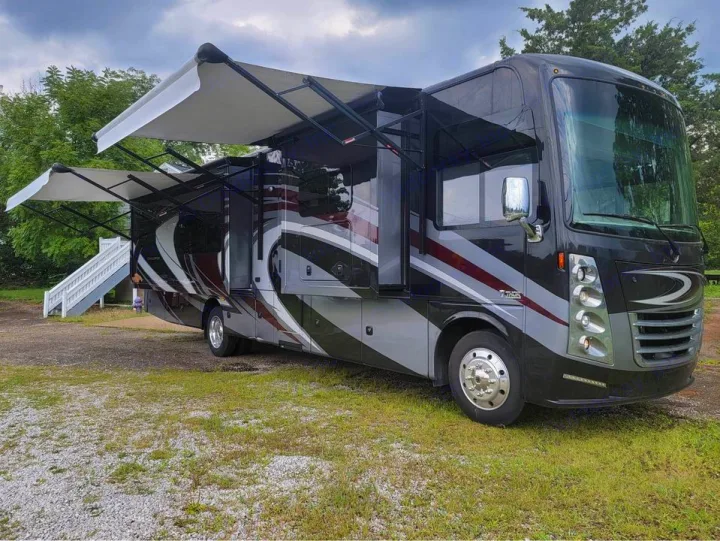 Black and grey RV with extended awnings & white stairs, parked on grass. Perfect for an rv rental road trip or camping getaway.. Thor Challenger 2019