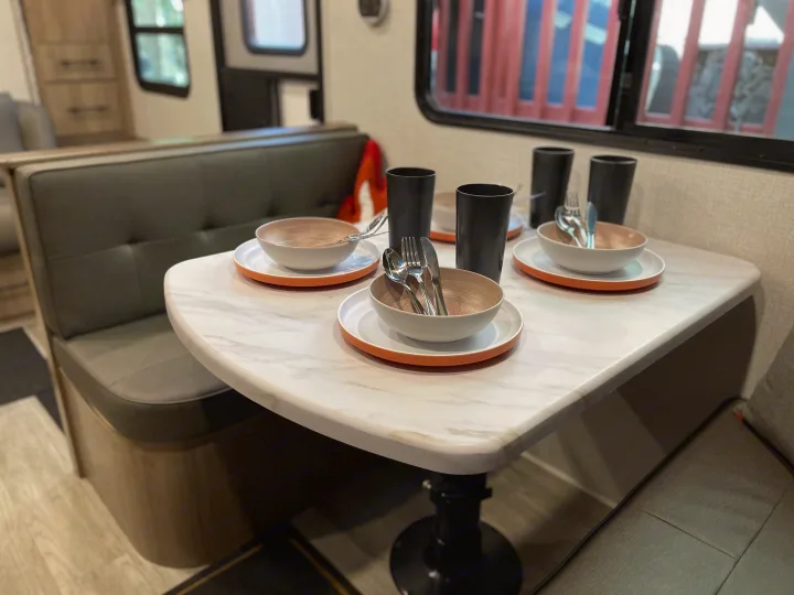 Modern RV rental dining area with a clean dinette, set with dinnerware, cups, and cutlery, ready for a meal.. Grand Design Imagine XLS 2023