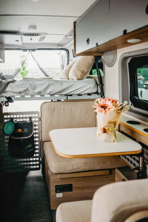 Modern rv rental interior: elevated bed, comfy dinette with table, overhead storage, and dog travel accessories visible.. Winnebago Solis Pocket 2022