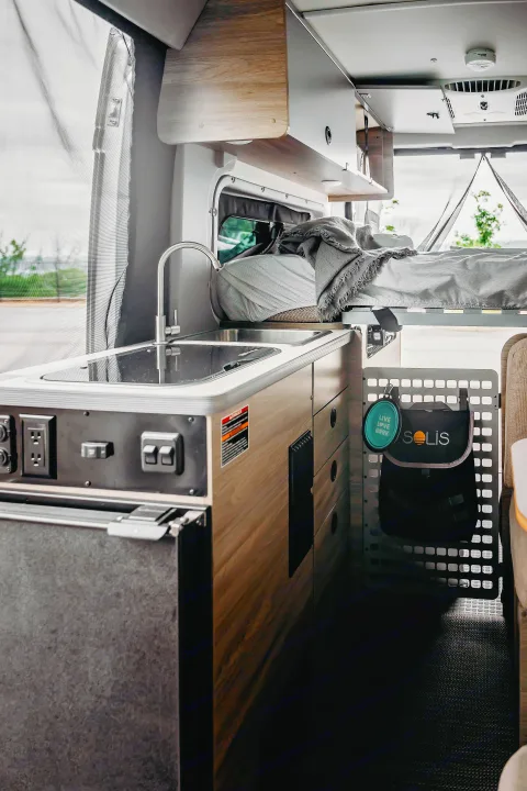 RV rental: Inside a modern camper van. Features a compact kitchen with sink, fridge, controls, and an elevated bed.. Winnebago Solis Pocket 2022