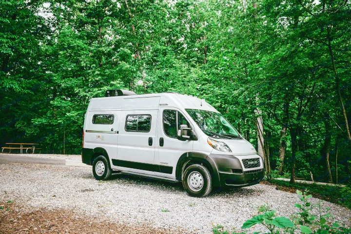 Explore nature in this gray Winnebago Solis Pocket rv rental, parked on gravel with green trees and a picnic table.. Winnebago Solis Pocket 2022