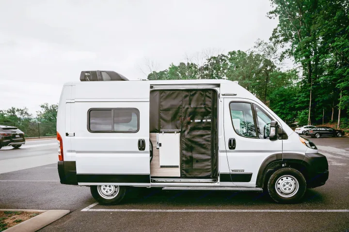 White Winnebago camper van RV rental, side door open showing a black screen and compact interior with fridge.. Winnebago Solis Pocket 2022
