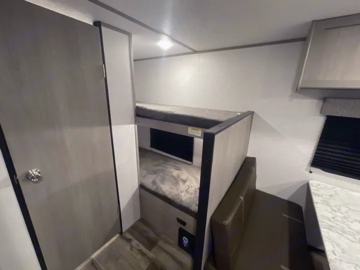 RV rental: Compact interior with two bunk beds, a brown dinette, and a table by a window. A door is on the left.. Coleman Other 2022