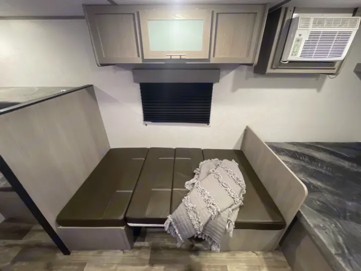 RV rental interior showing a dinette with green cushions, a blanket, overhead cabinets, and an AC unit.. Coleman Other 2022