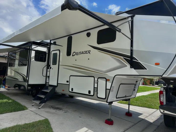 Large white Crusader fifth-wheel RV rental parked with awning extended, slide-outs open on sunny driveway.. Crusader Crusader Fifth Wheel 2022