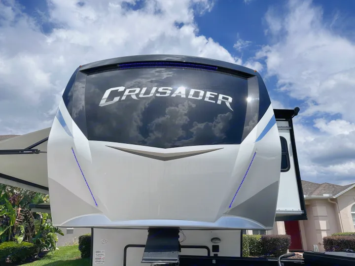 Up-close of a Crusader fifth-wheel RV's sleek front cap with blue lights & sky reflections. Envision your next rv rental!. Crusader Crusader Fifth Wheel 2022