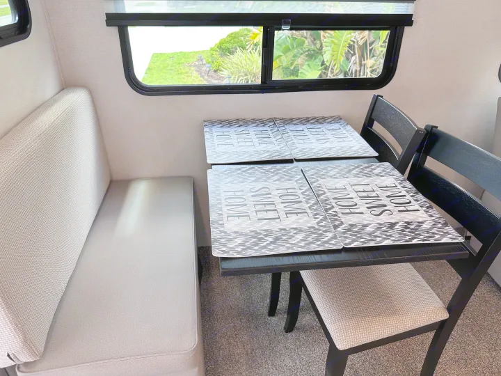 Cozy RV rental dining area with a booth, table, and chairs. Features 'Sweet Home' placemats and views of greenery.. Crusader Crusader Fifth Wheel 2022