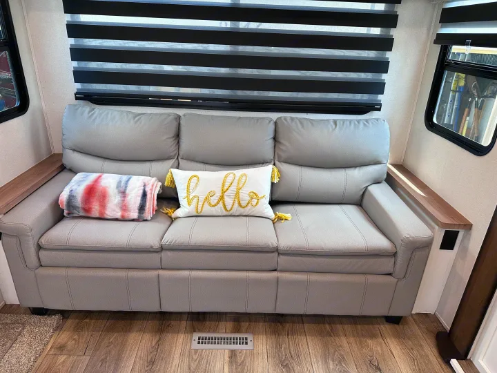 Plush gray sofa in an RV rental, complete with a cozy blanket, "hello" pillow, and striped window blinds.. Crusader Crusader Fifth Wheel 2022