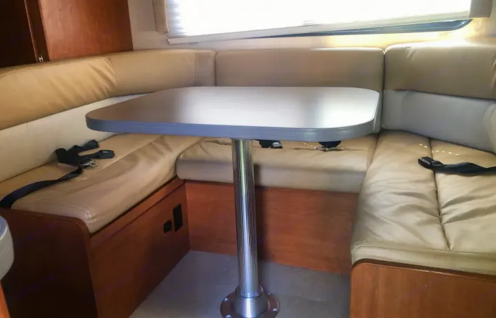 Spacious U-shaped dinette in an RV rental, with light cushioned seating, a central table, and visible seatbelts.. Winnebago Minnie Winnie 2016