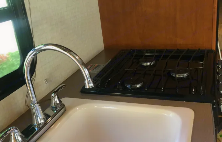 RV rental kitchen: A compact space with a chrome faucet, white sink, and three-burner gas stovetop for your travels.. Winnebago Minnie Winnie 2016