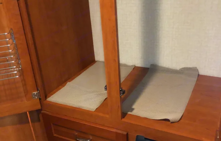 RV rental cabinet interior with anti-slip mats on wooden shelves and a door rack for organized storage.. Winnebago Minnie Winnie 2016