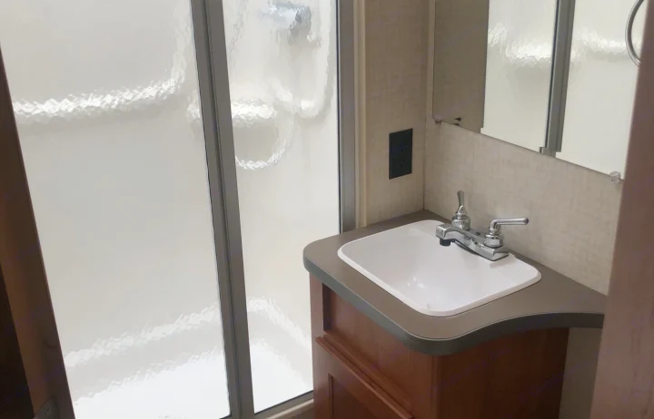 Experience comfort in this RV rental bathroom with a clean sink, vanity, frosted shower, and mirror.. Winnebago Minnie Winnie 2016