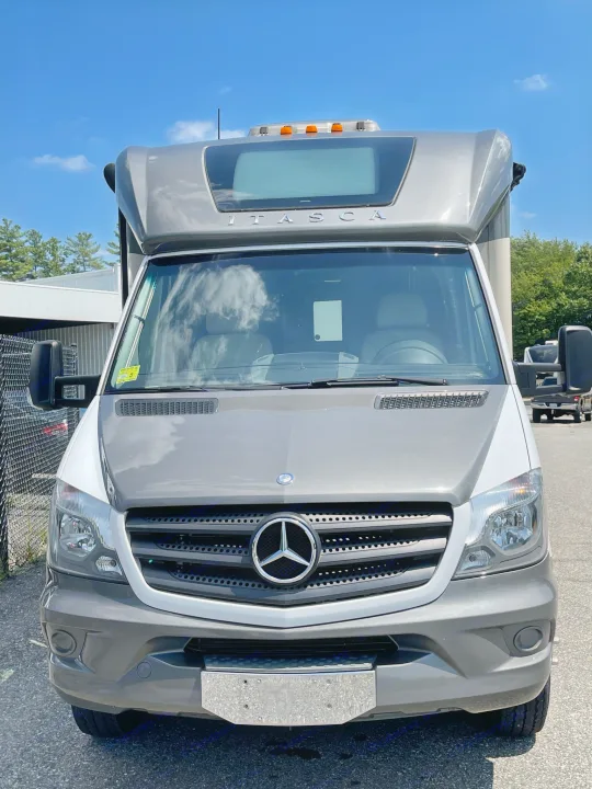 Front view of a gray and white Mercedes-Benz Sprinter-based Itasca RV rental, parked under a blue sky.. Itasca Navion 2015