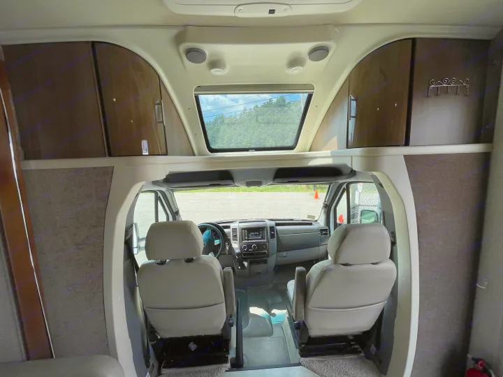 Explore this RV rental's inviting interior! Features a spacious cockpit, overhead area with skylight, and ample storage.. Itasca Navion 2015