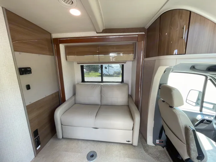 RV rental interior with a light sofa, window, overhead cabinets, and front cabin.. Itasca Navion 2015