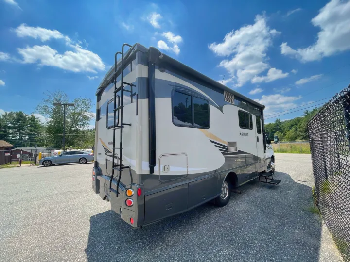 This grey and white Class C RV rental, equipped with a rear ladder, is parked outdoors on a clear day.. Itasca Navion 2015