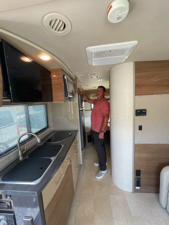 Spacious RV rental interior featuring a man, kitchen area with sink, TV, and modern amenities for comfortable travel.. Itasca Navion 2015