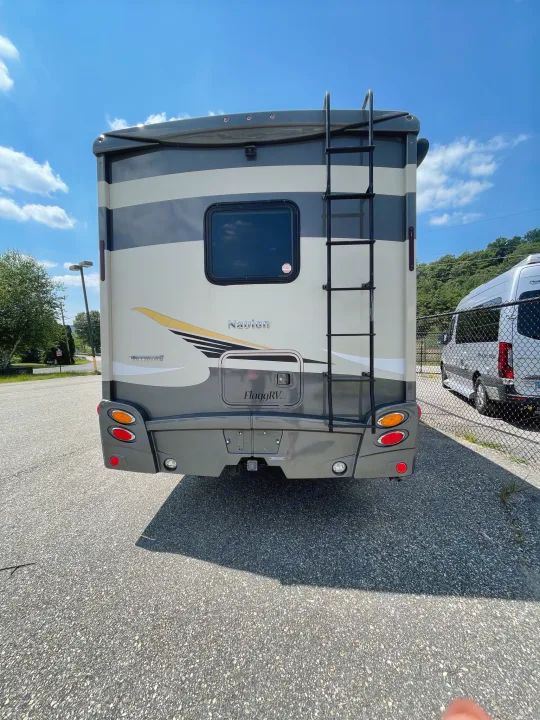 Rear view of a beige & grey Winnebago Navion motorhome, parked with a ladder on back, suitable for rv rental.. Itasca Navion 2015