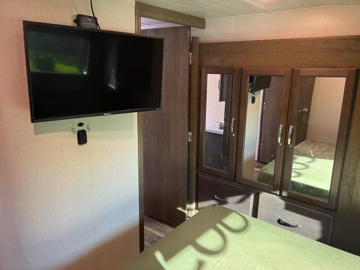 An RV rental bedroom showcasing a wall-mounted TV, mirrored wardrobe, and part of the bed for a compact living space.. Keystone RV Cougar 364 BHL 2022
