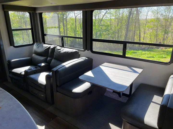 Spacious RV rental interior with black recliners and a dining area, brightly lit by large windows offering nature views.. Keystone RV Cougar 364 BHL 2022