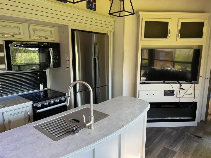 Modern RV rental kitchen and living area, featuring full appliances, entertainment, and fireplace for comfortable travel.. Keystone RV Cougar 364 BHL 2022